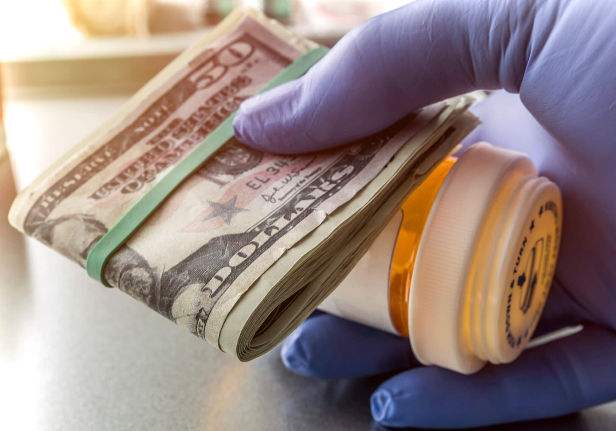 Hand in latex glove holds prescription drug bottle and roll of dollar bills