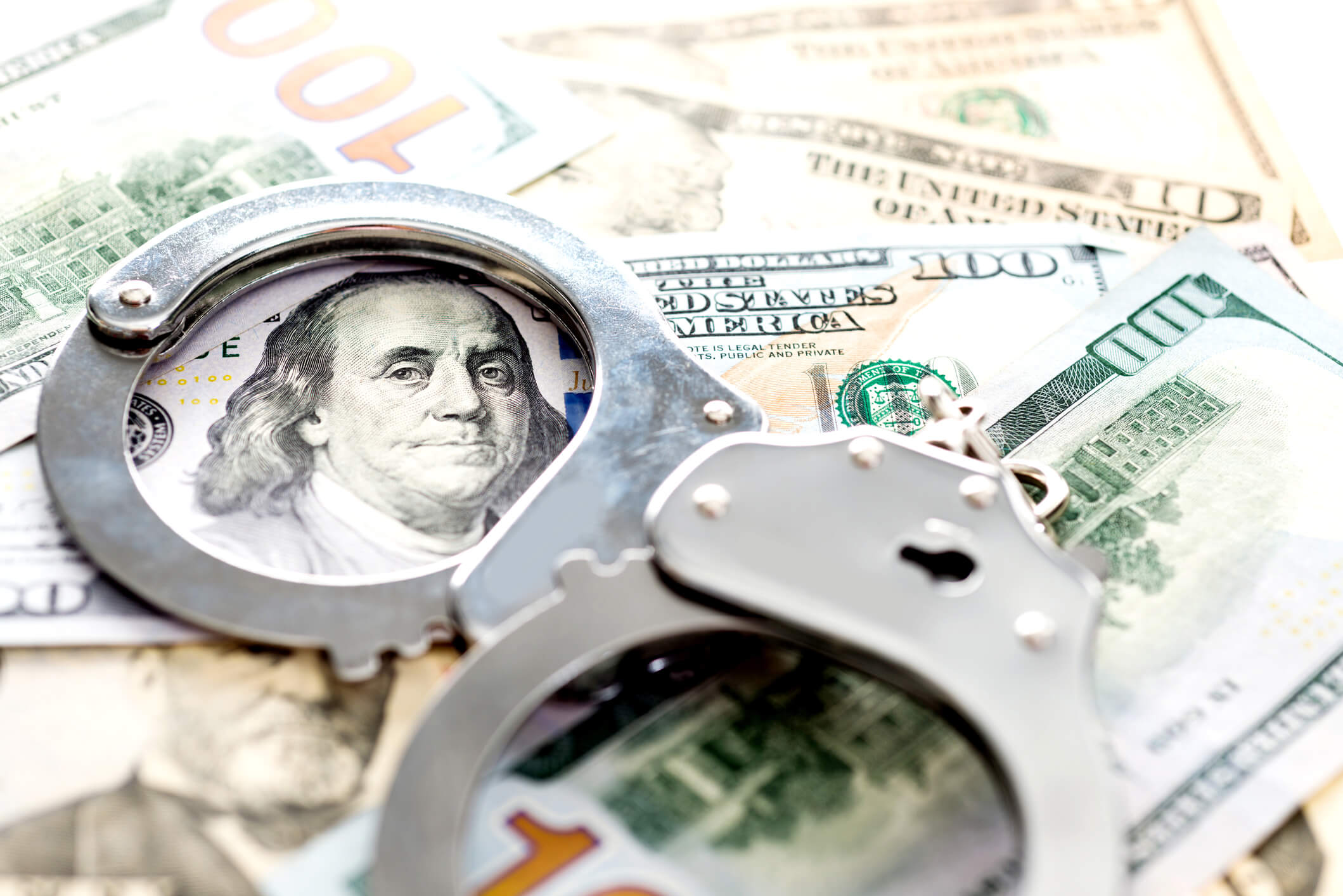 Handcuffs laying on top of a pile of money, a concept of grand larceny.