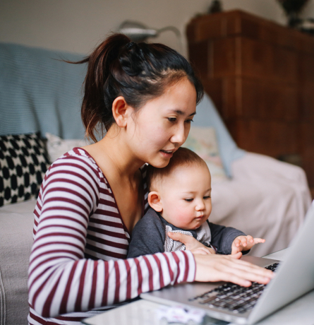 Mother uses laptop with her baby on her lap